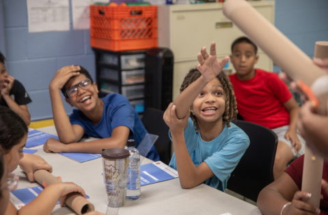 Smiling child in a blue shirt eagerly raises his hand